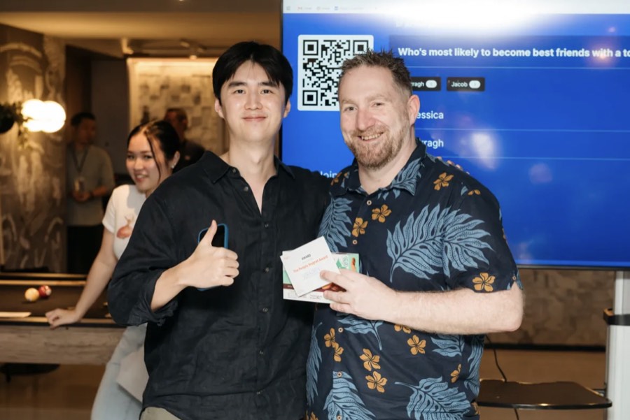 Two teammates smiling and holding a printed 'People's Award' card